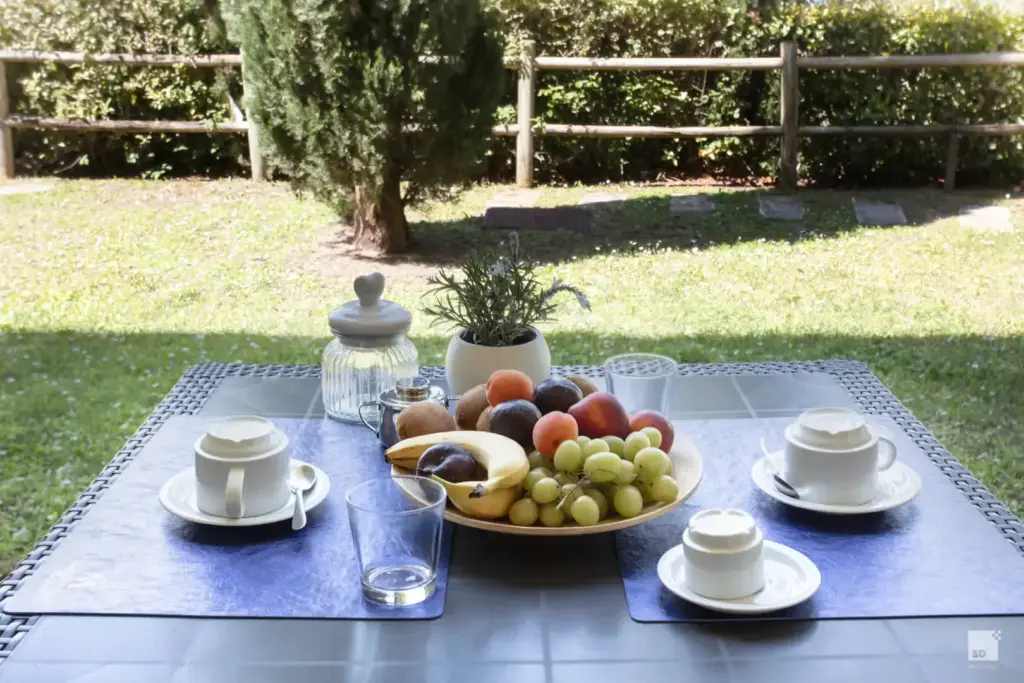 Tavolo apparecchiato per la colazione all'aperto con frutta fresca e tazzine da caffè nel giardino del Chianti Village Morrocco.